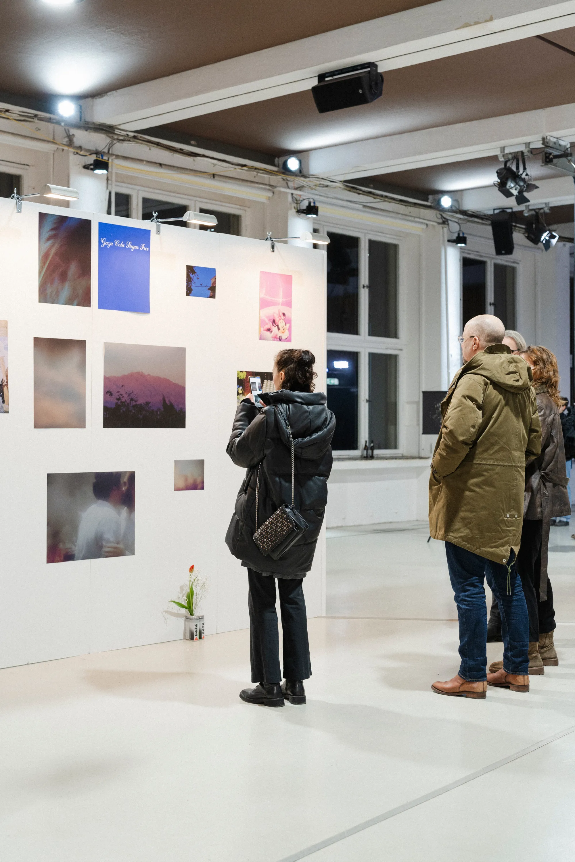 Das Bild zeigt die Ausstellungsansicht des ersten Rundgangs der Jüdischen Kunstschule. Besucher:innen betrachten Fotografien unterschiedlicher Formate an einer weißen Galeriewand in modernen Ausstellungsräumen.