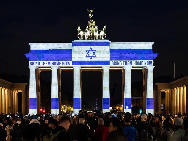 Das Bild zur Studie Deutsch-Israelischer Kulturbeziehungen zeigt das Brandenburger Tor bei Nacht mit Projektion der israelischen Flagge und dem Text »BRING THEM HOME NOW«, umgeben von einer Menschenmenge.