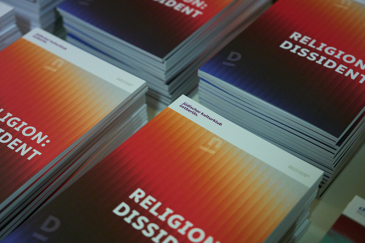 Das Bild zeigt mehrere Stapel von der vom Institut veröffentlichten Publikation »Religion: Dissident«. Das Cover hat einen durch bunte Streifen illustrierten Farbverlauf.
