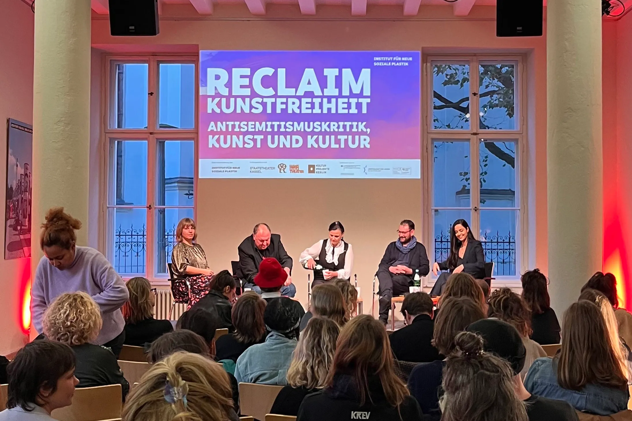 Podiumsdiskussion zur Abschlussveranstaltung vom Projekt »Reclaim Kunstfreiheit: Antisemitismuskritik, Kunst und Kultur«. Zu sehen sind fünf Personen vor Publikum, mit einer großen Projektion im Hintergrund.